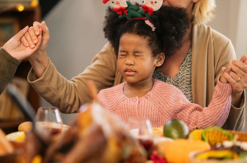 Girl praying with her family before Christmas dinner.